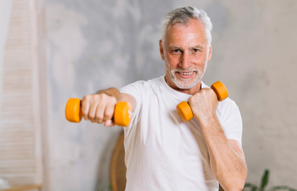 Smiling and confident older man lifting orange dumbbells in a serene indoor setting, symbolizing strength, hormonal balance, and essential care for prostate health, promoting a fulfilling and active life for all ages.