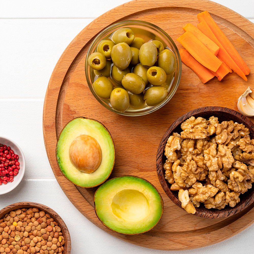 Round plate with sliced avocado, nuts, olives, carrots, and lentils on light wood.