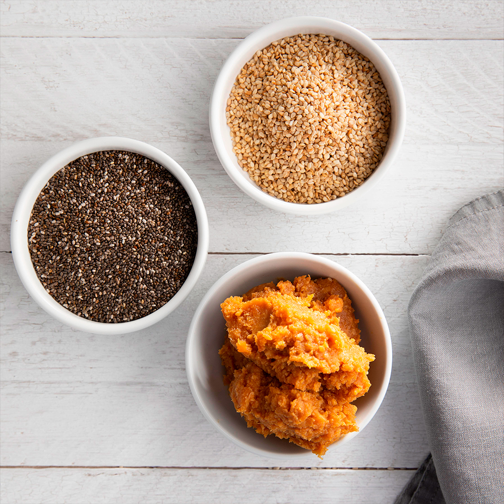 Bowls of quinoa, chia seeds, sesame, and pumpkin paste in minimalist white porcelain.