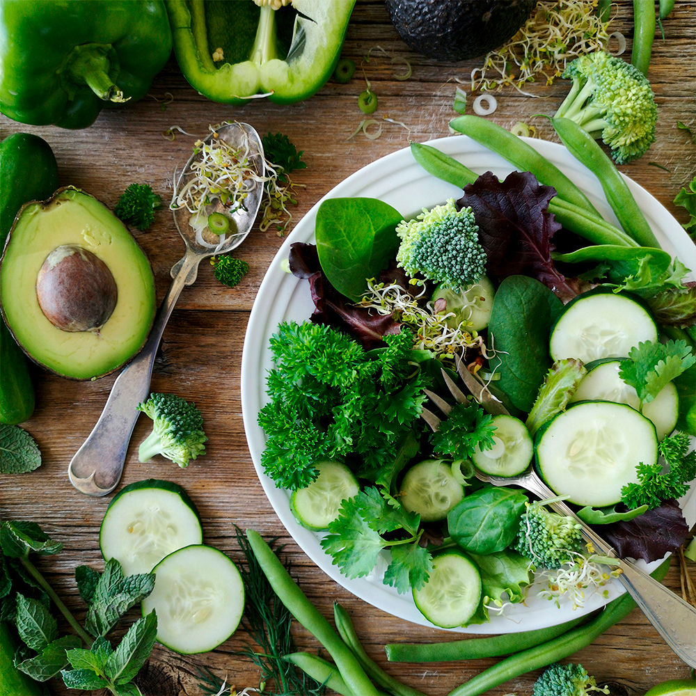 Fresh green leafy salad with spinach, lettuce, broccoli, avocado, and cucumber on a wooden plate.