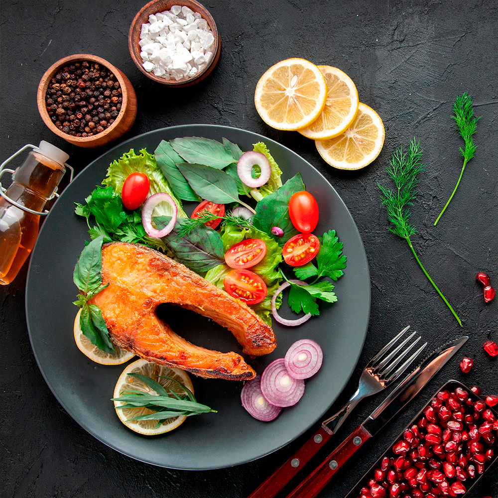 Grilled salmon plate with lemon, cherry tomatoes, and fresh herbs on a textured dark background.