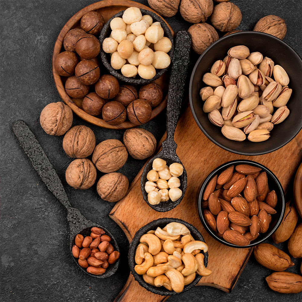 Variety of nuts like almonds, Brazil nuts, pistachios, and macadamias on textured dark plates.