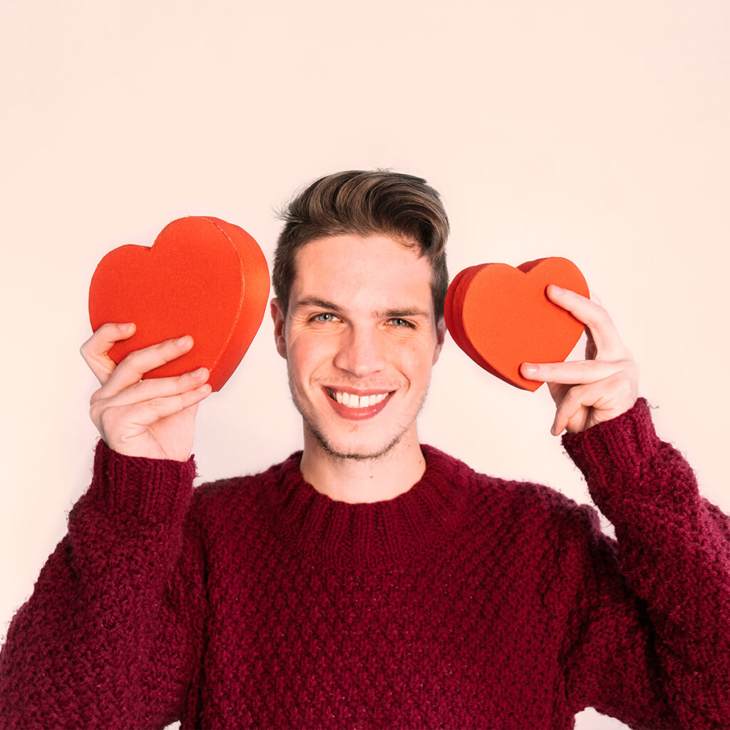 Smiling man holding red hearts, symbolizing magnesium that relaxes muscles, relieves stress, and cares for the heart.