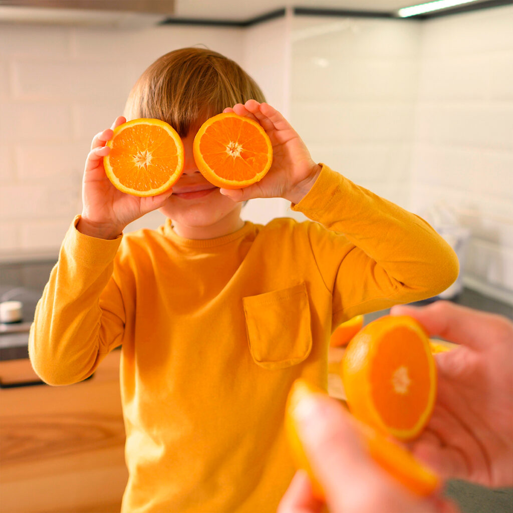 A child holding orange slices over their eyes, representing the immune and skin benefits of Vitamin C